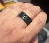 Hand wearing a black ring with a tire tread pattern