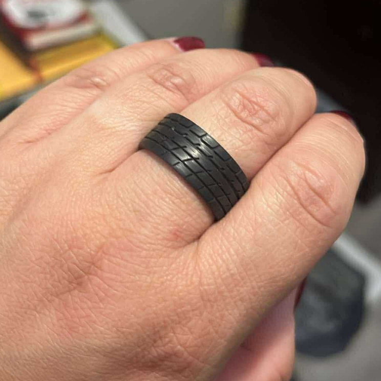 Hand wearing a black ring with a tire tread pattern